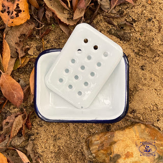 Enamel soap dish on sand with leaves with the upper tray at an angle