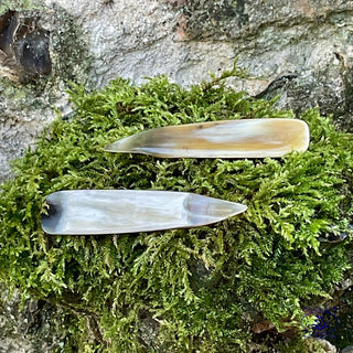 the front and back of a horn manicure predicure tool on moss